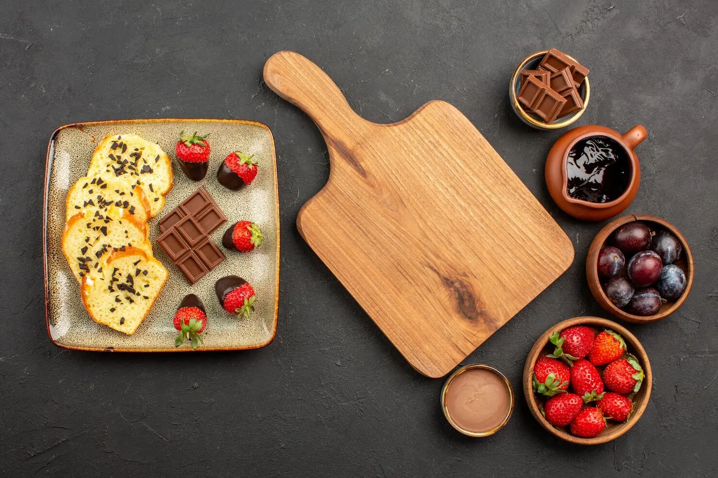 top-view-cake-strawberries-wooden-board-pieces-cake-with-chocolate-left-bowls-with-strawberries-berries-chocolate-sauce-right-side-table_140725-117481